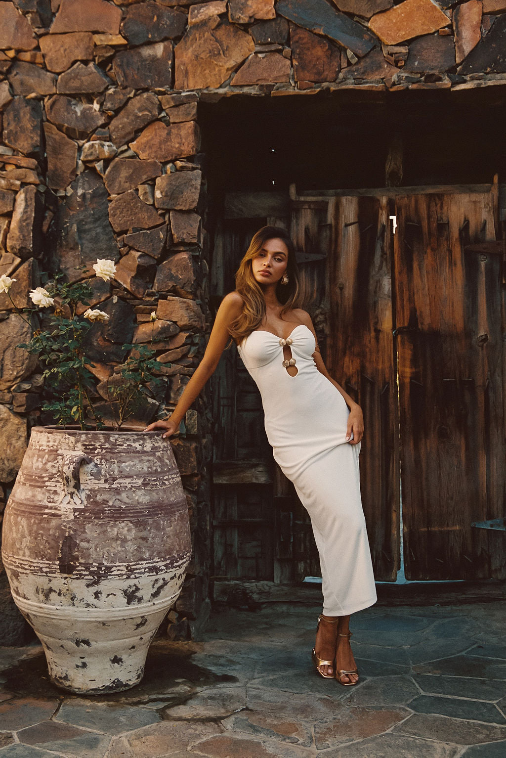 Model wearing the 12th Tribe Rayne White Embellished Maxi Dress in a new color way, featuring gold shell detailing with a flowing maxi silhouette for an elegant resort ready look.