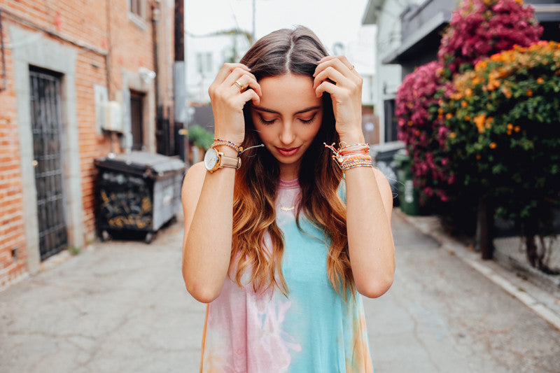 Person in pastel tie dye tank dress wears stacked Pura Vida bracelets in an alley.