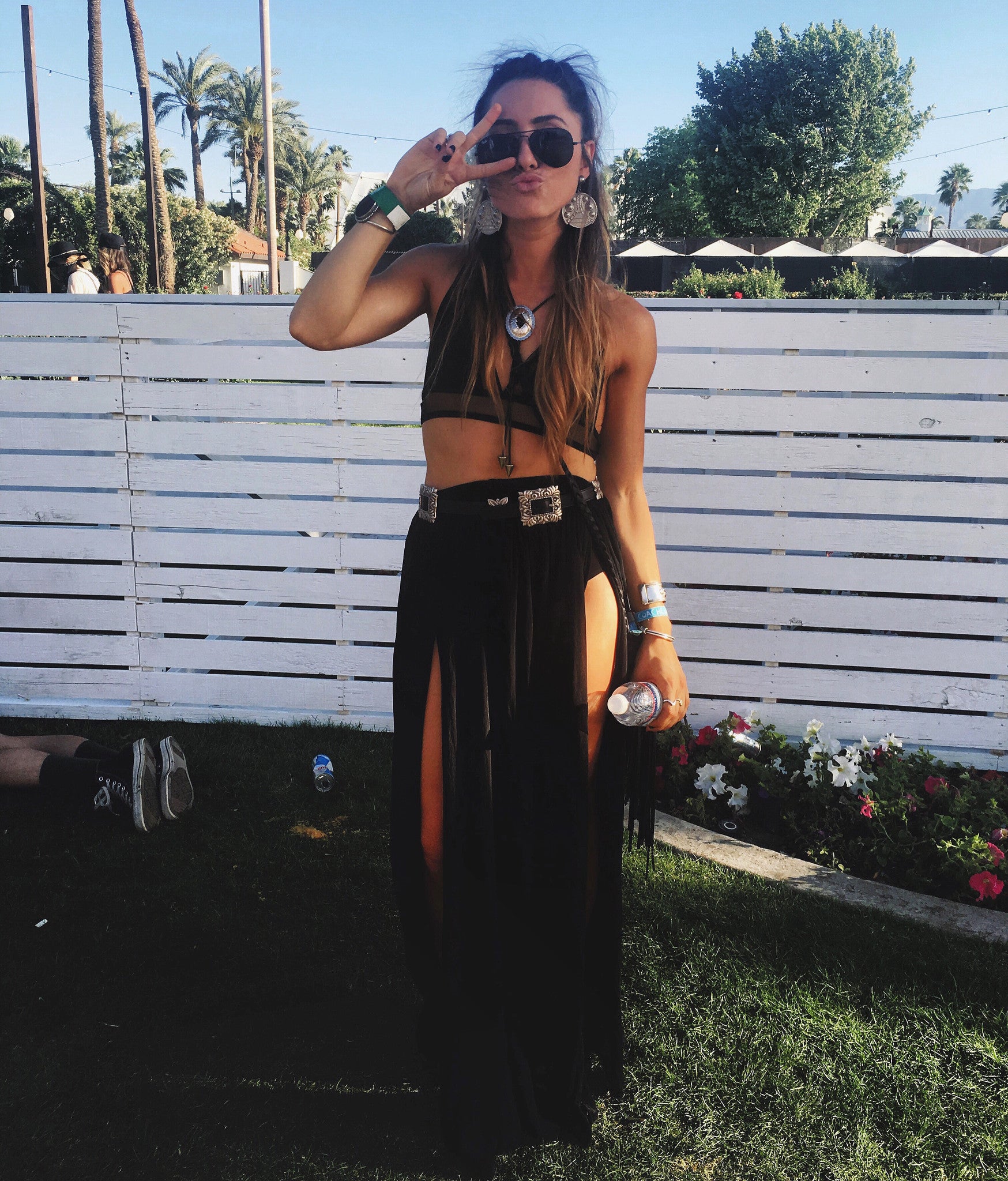 Festival-goer in black crop top and high-slit maxi skirt poses at Coachella among palm trees.
