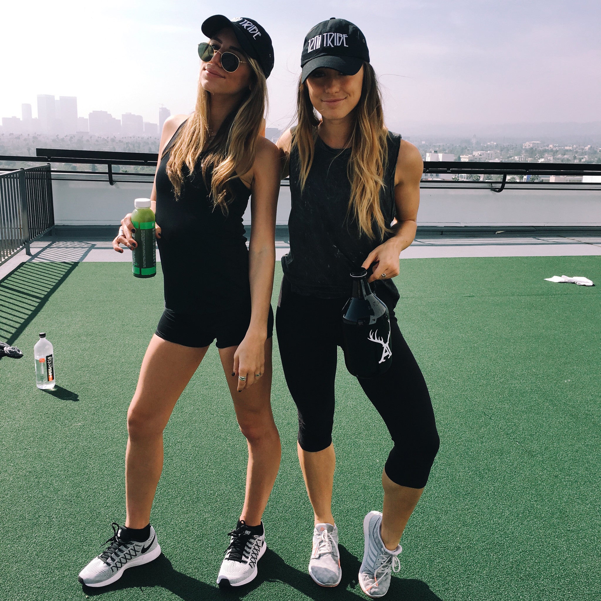 Two people in black 12th Tribe caps and activewear on a rooftop overlooking the LA skyline.