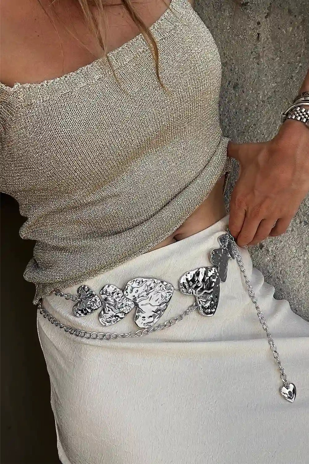 Silver heart statement belt with embossed heart-shaped buckles and dangling chain detail on white pants.