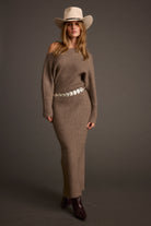 Woman wearing a brown knit outfit with a belt and cowboy hat on a gray background