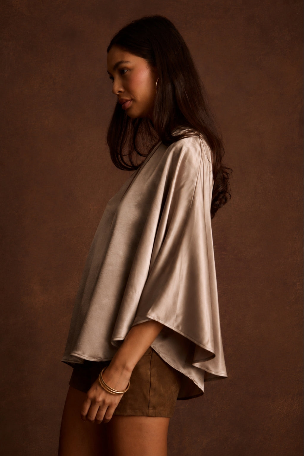Profile view of a woman wearing a draped champagne satin one-shoulder top with brown shorts