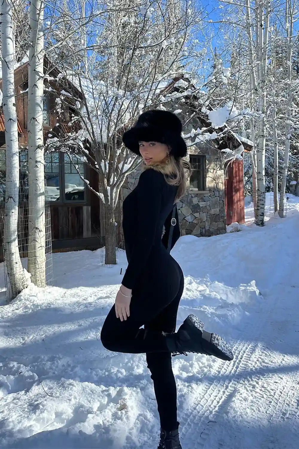 Black faux fur trimmed jumpsuit styled with a matching fur hat in a snowy winter setting.