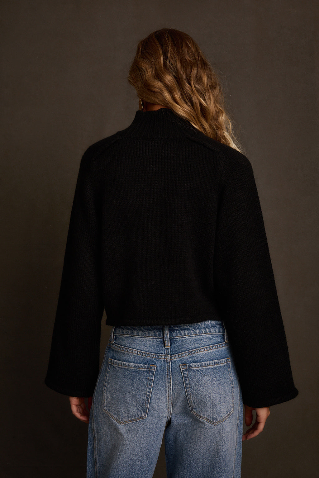 Black sweater back view showing clean mock neck and relaxed bell sleeve silhouette