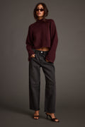 Woman in sunglasses wearing a plum cropped turtleneck sweater with washed black barrel-leg jeans and black strappy heels.