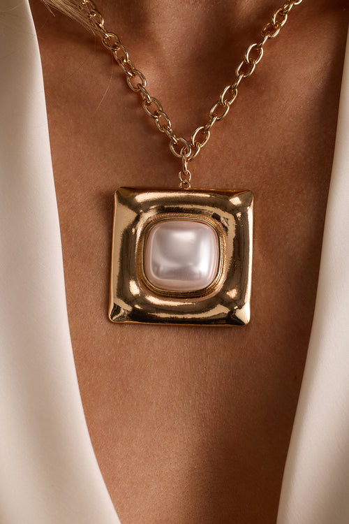 Close-up of a gold chunky chain necklace with a square pearl pendant on a chiseled gold frame.