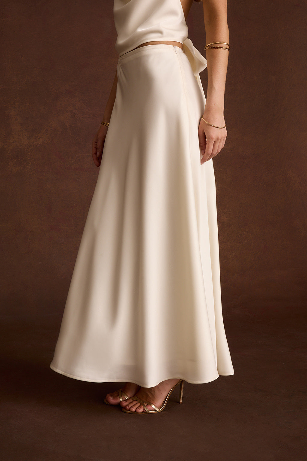 Side view of an ivory satin maxi skirt with a fitted waistband and flared hem.