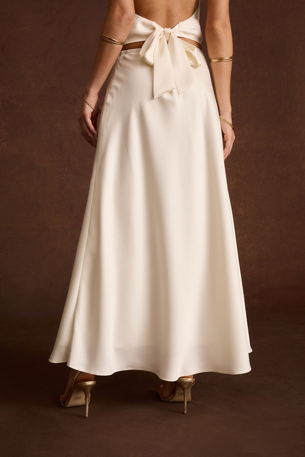 Back view of an ivory satin maxi skirt with a tie-back bow detail at the waist.