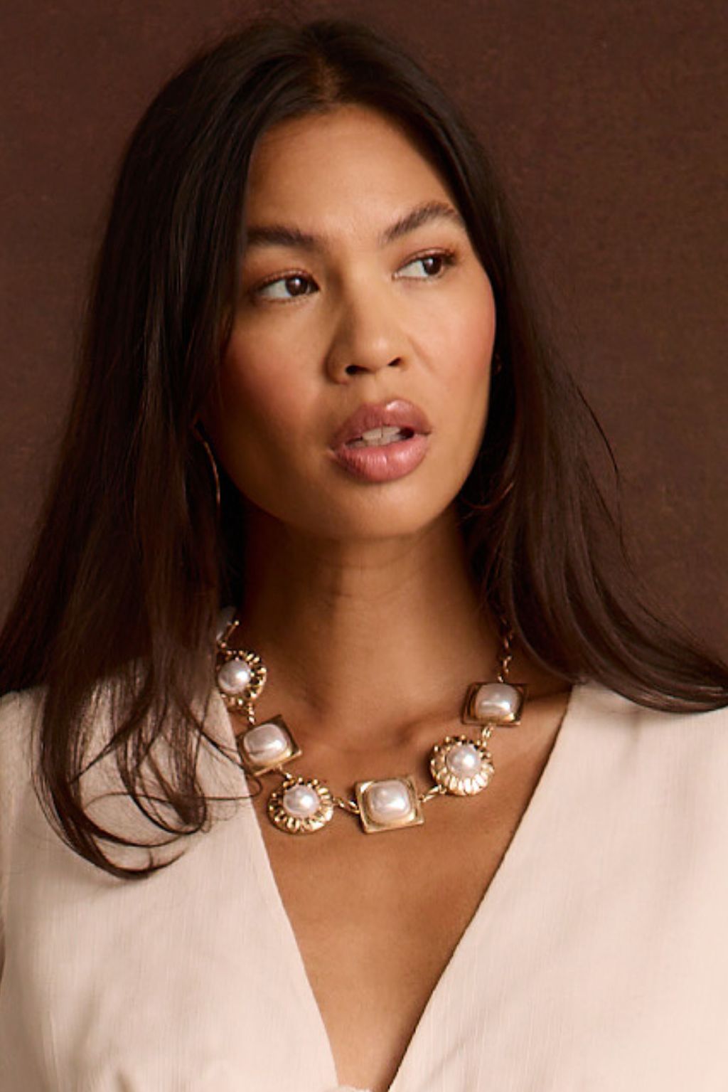 Close-up of a woman wearing a chunky pearl and gold statement choker necklace with a beige blouse