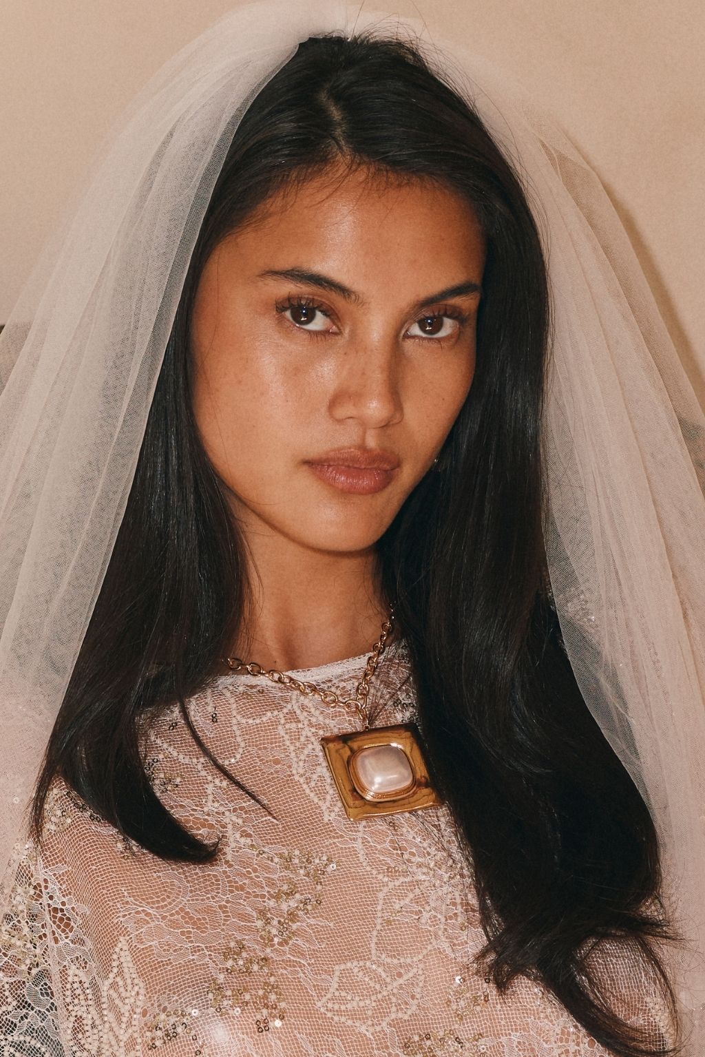 Bride wearing a gold statement necklace with a pearl pendant and a tulle veil