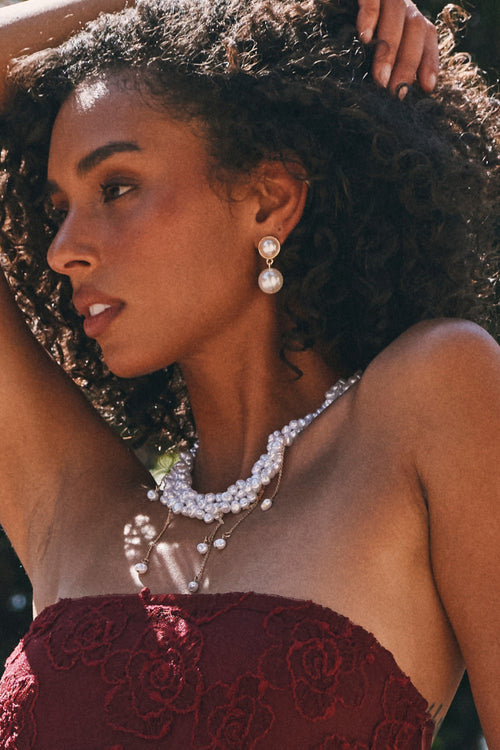 Double pearl drop earring with a round pearl top and larger pearl bottom, paired with a layered pearl necklace.