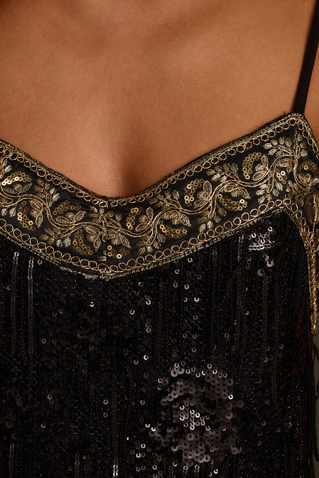 Black sequin fabric detail showing fringe texture and gold embellishment close-up