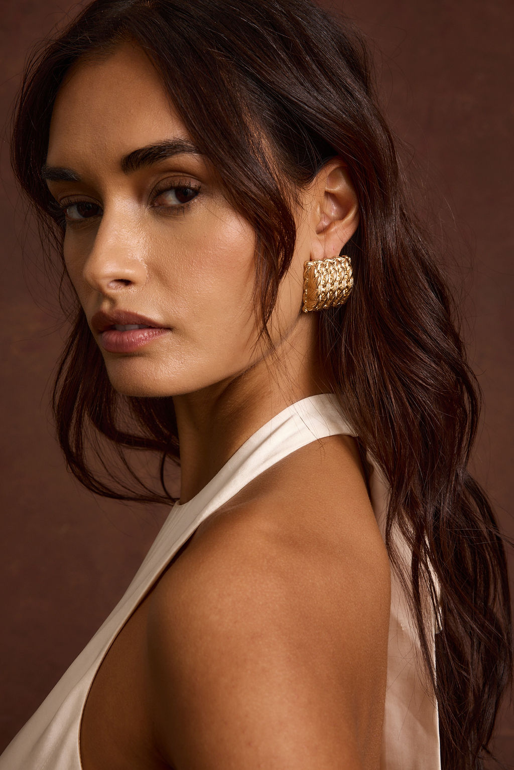 Model wearing the 12th Tribe Calaia Gold Earrings, featured in a gold-tone in a statement design, styled with the Saltwater Ivory Satin Maxi Dress.