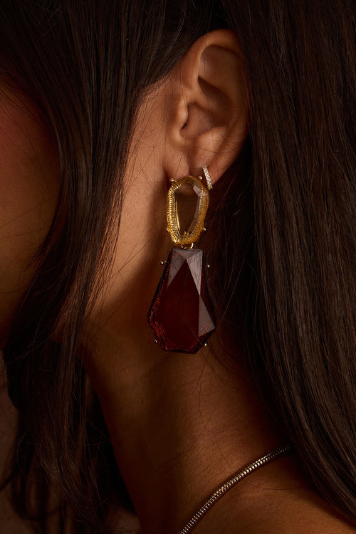 Gold statement drop earrings with a hammered open loop and a large faceted garnet-red crystal.