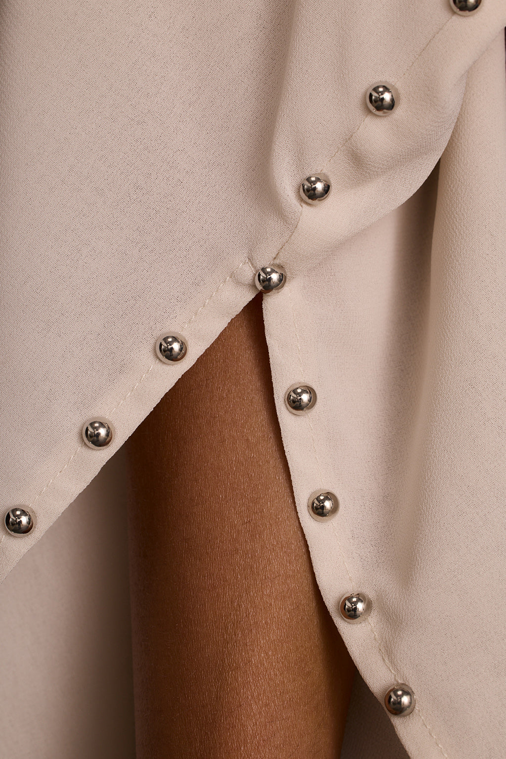 Detail shot of large silver ball studs along the side slit of a cream studded crop top