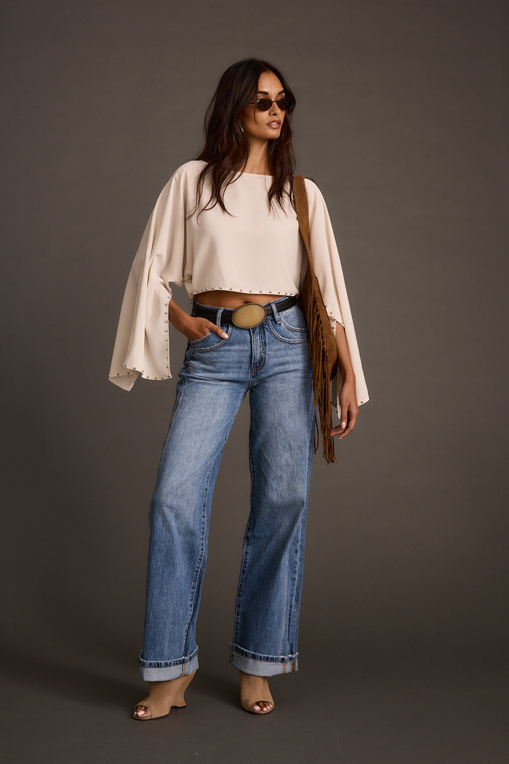 Woman styling a cream studded crop top with wide-leg jeans, a fringe bag, and heeled sandals