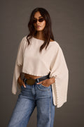 Front view of a woman in a cream studded off-shoulder top and wide-leg blue jeans