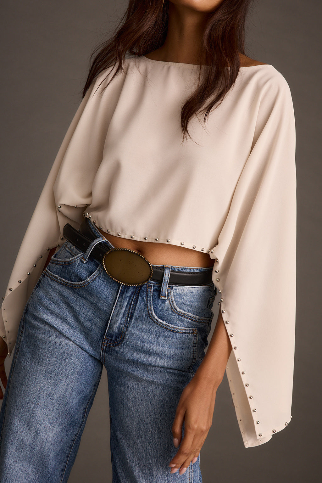 Close-up of a cream studded crop top paired with a black belt and wide-leg blue jeans
