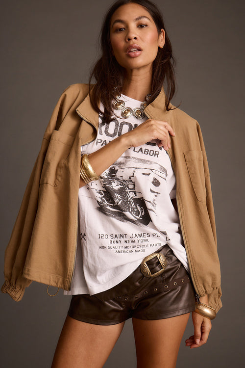 Woman posing in brown vegan leather shorts and a tan utility jacket over a graphic t-shirt
