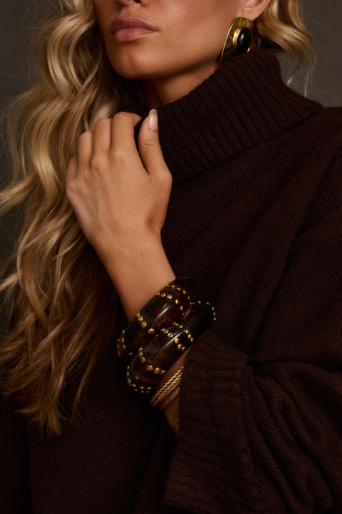 Studded bangle set in tortoise resin with gold stud accents, worn stacked on wrist with turtleneck