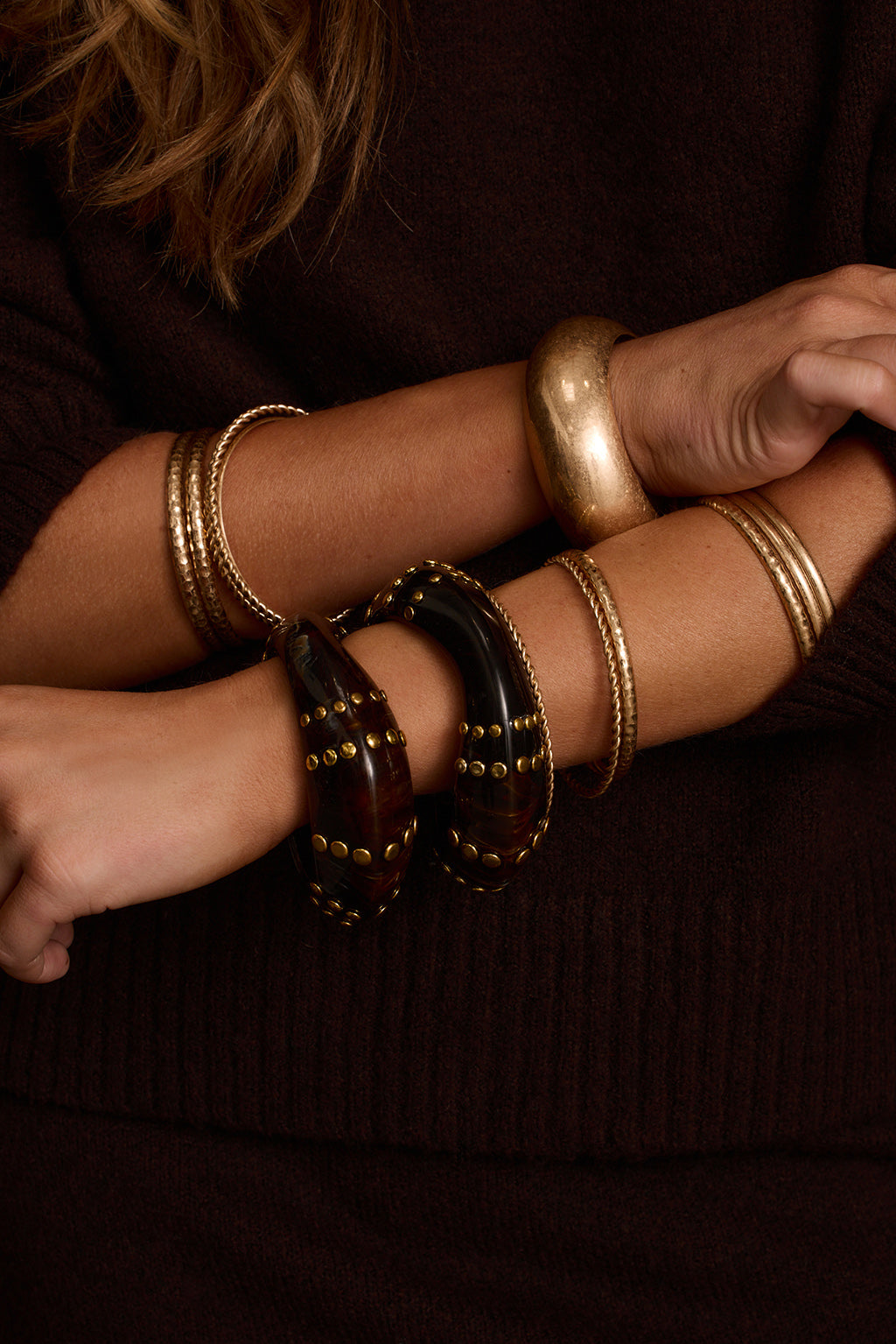 Statement bangles styled with espresso sweater, gold cuff, and gold earrings