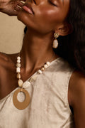 Close-up of hammered gold drop earring with ivory stone, worn with beaded pendant necklace.