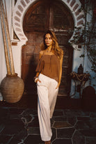 Model wearing the 12th Tribe Moonlit Kiss Cream Satin Trousers, styled with the Costella Mocha Asymmetrical Top, Soreya Resin and Gold Bangles, and Calaia Gold Earrings, featuring a mid rise fit, wide-leg satin silhouette for an elegant, flowing fit