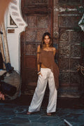 Model wearing the 12th Tribe Costella Mocha Asymmetrical Top, featuring a flowy silhouette sheer material, styled with the Moonlit Kiss Cream Satin Trousers, Soreya Resin and Gold Bangles, and Calaia Gold Earrings