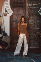 Model wearing the 12th Tribe Costella Mocha Asymmetrical Top, featuring a flowy silhouette sheer material, styled with the Moonlit Kiss Cream Satin Trousers, Soreya Resin and Gold Bangles, and Calaia Gold Earrings