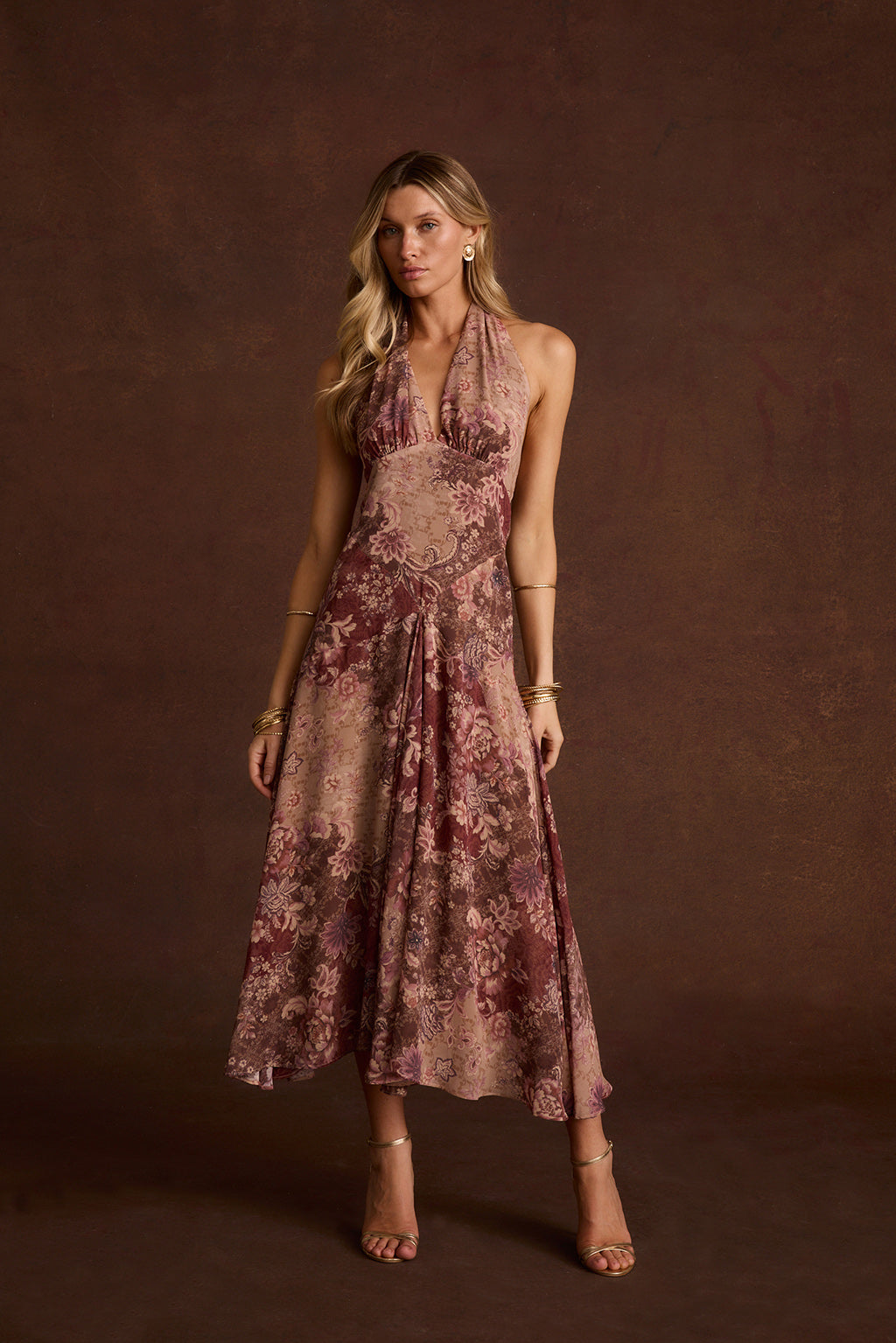 Person in Darcy berry floral chiffon halter maxi dress with gold heels and bangles.