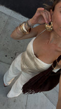 Cream satin corset top and matching wide-leg trousers styled with gold bangles and a fringe shoulder bag