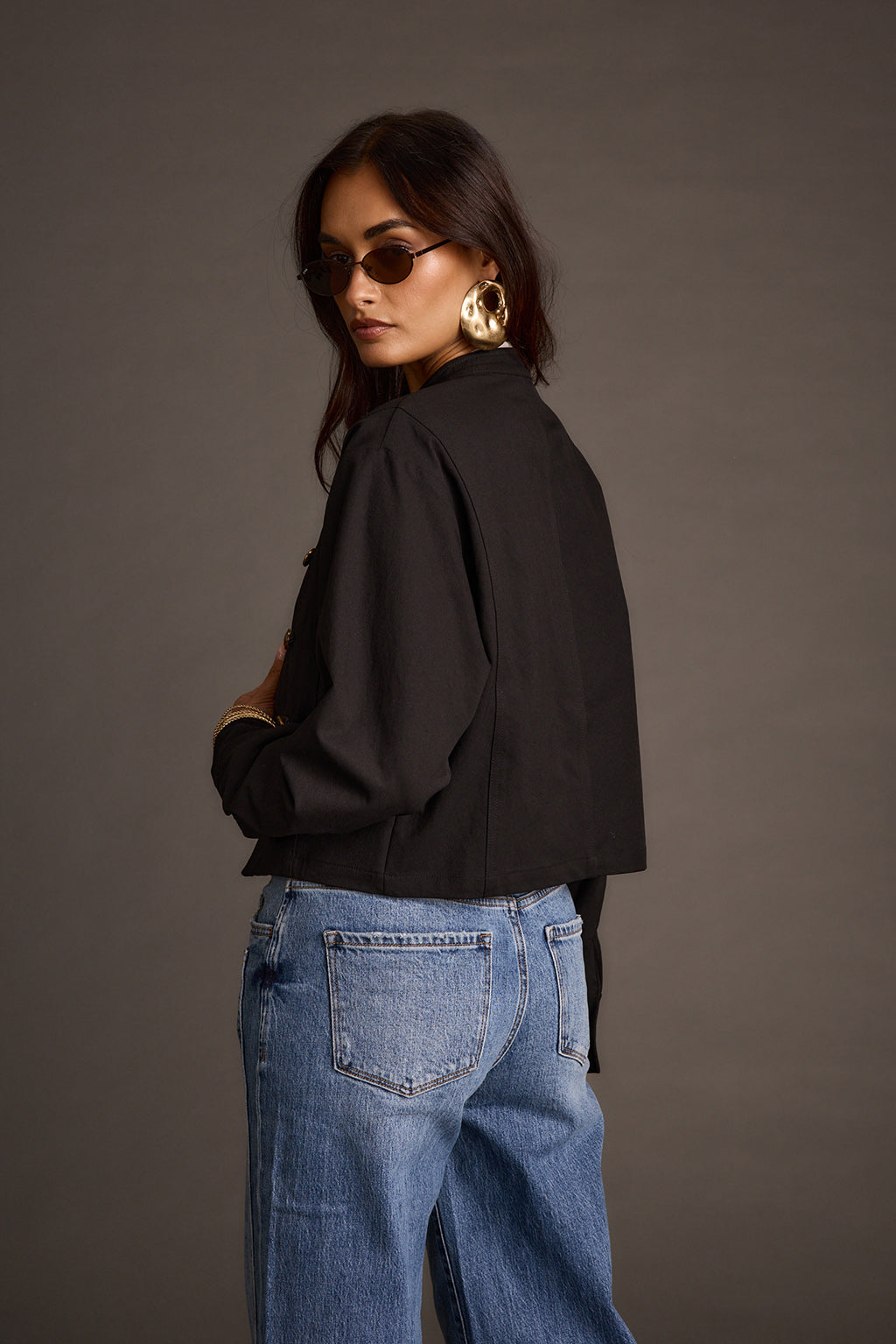 Back view of a woman in a black cropped drummer jacket and wide-leg denim jeans