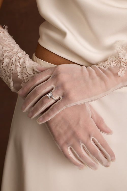 Sheer white lace trim bridal gloves worn with a solitaire ring over satin.