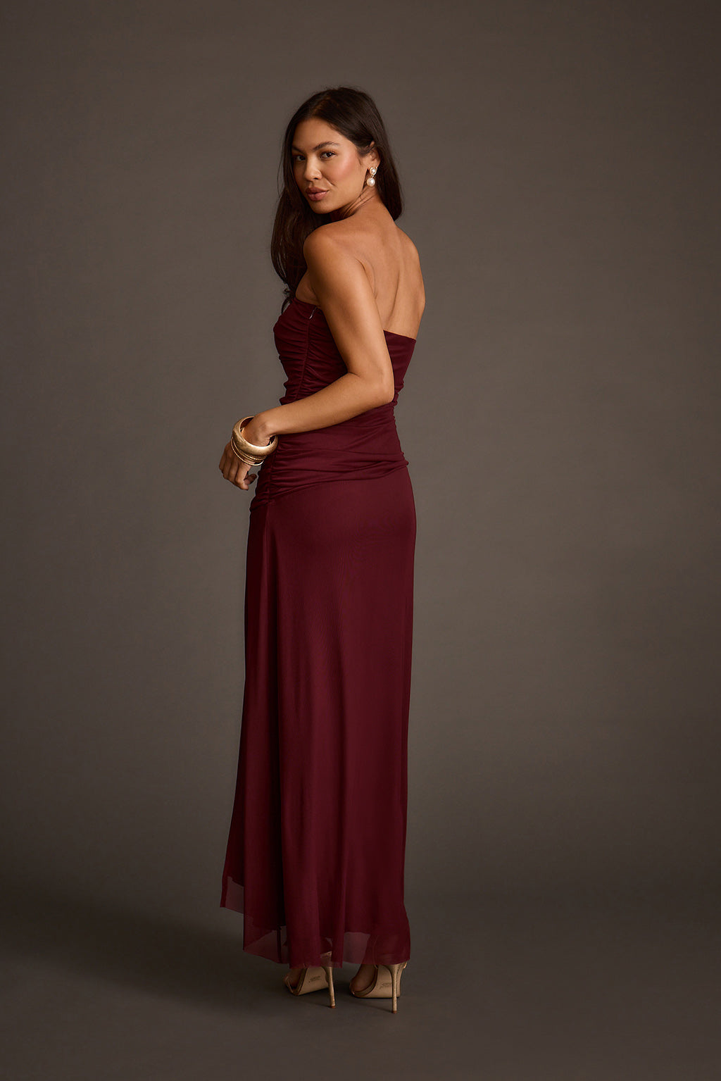 Back view of a burgundy strapless mesh maxi dress with an open back and ruched bodice.