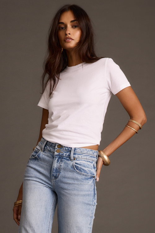 Woman modeling a white crewneck t-shirt tucked into light-wash jeans with gold bracelets.