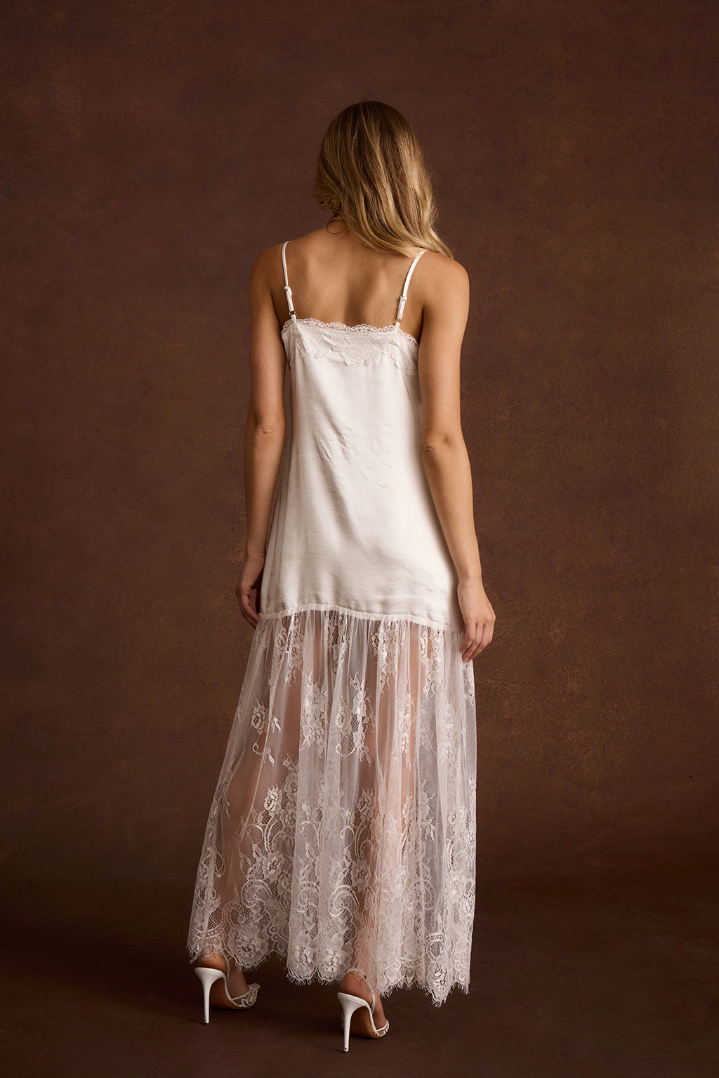Back view of a white satin slip dress with a lace trim neckline and adjustable straps.