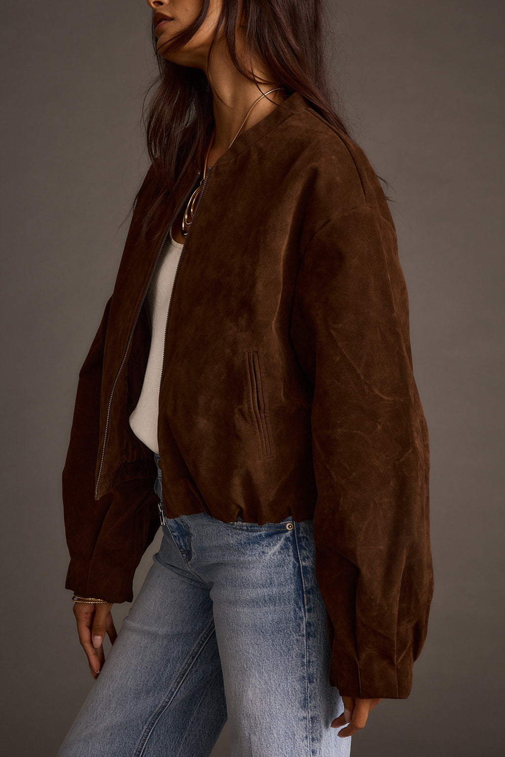Woman wearing mocha vegan suede jacket over white top with blue jeans, side view