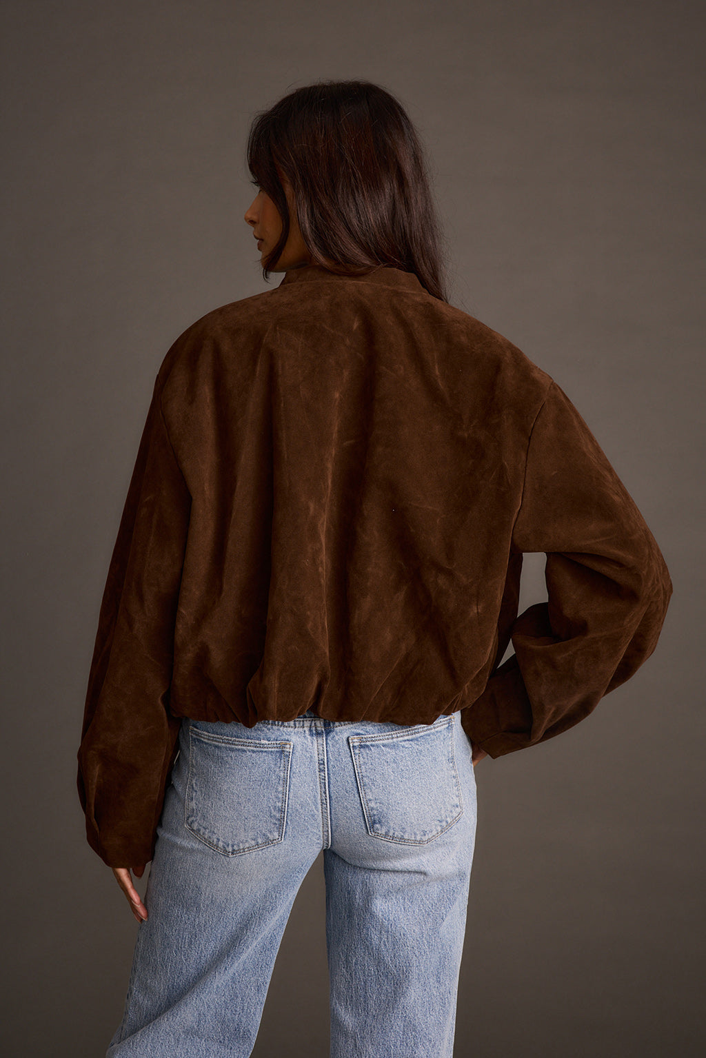 Woman wearing mocha vegan suede jacket with light-wash jeans, back view