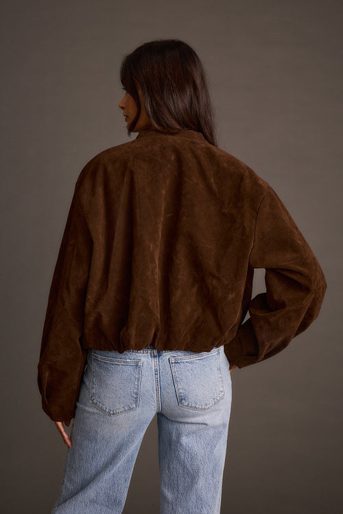 Woman wearing mocha vegan suede jacket with light-wash jeans, back view