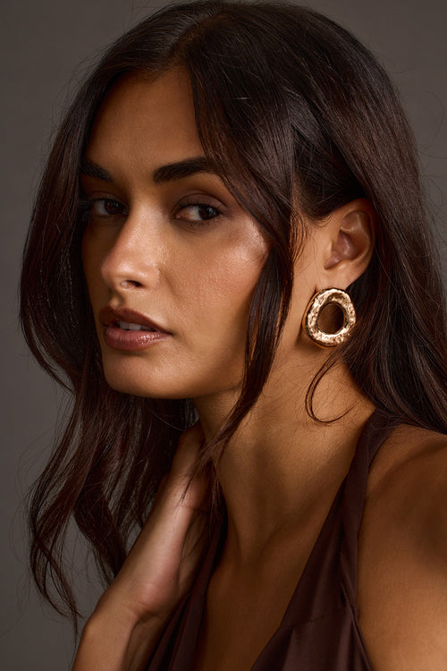 Woman wearing gold statement earrings with textured hoop design, close-up portrait