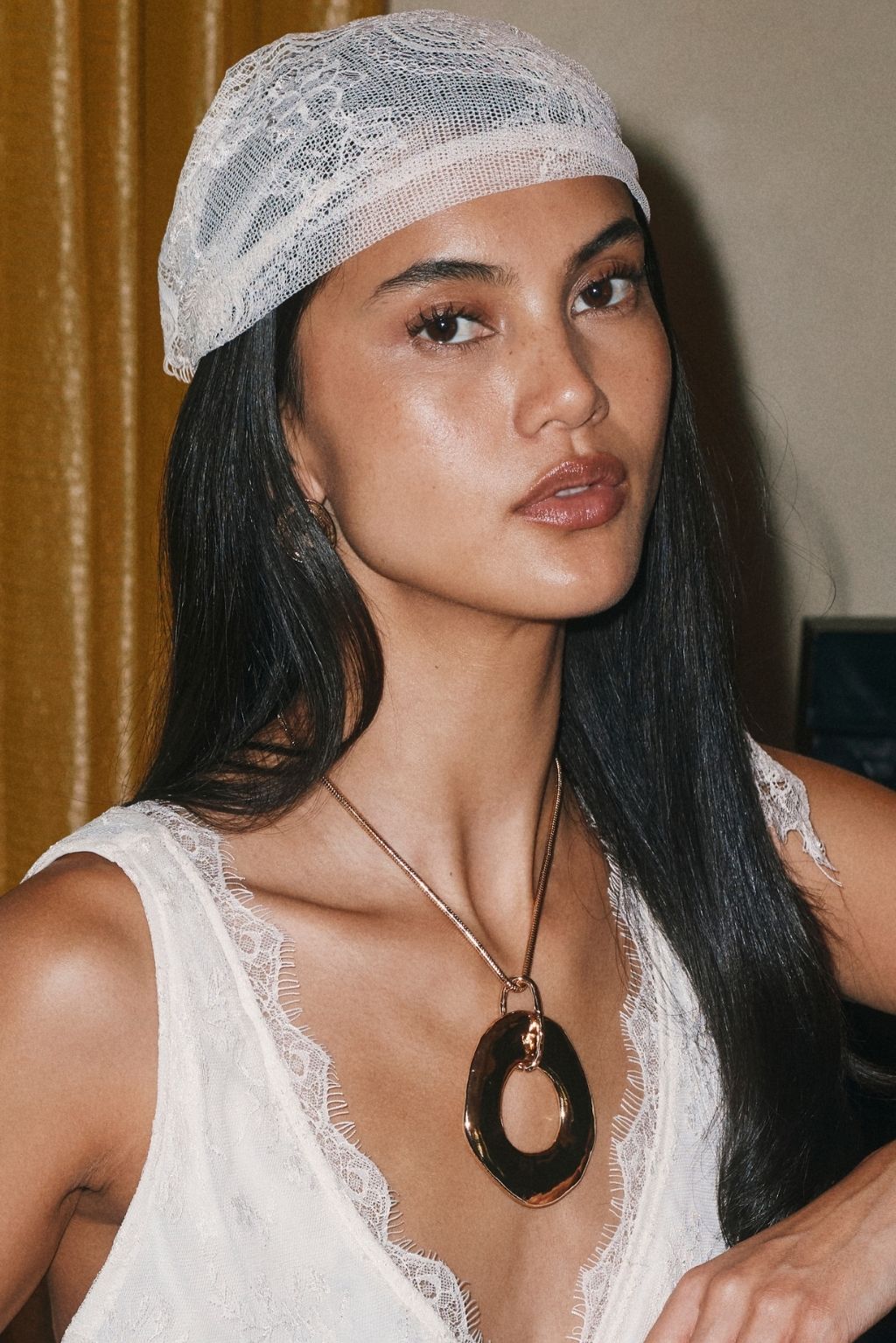 Woman wearing a gold pendant necklace with a large open oval dark tortoise-shell pendant and a white lace top