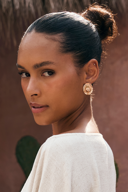 Model wearing the 12th Tribe Golden Dune Coin Earrings, textured gold coin earrings with a push-back closure, perfect for adding a bold, statement touch to festival-ready looks, summer soirées, and stylish warm-weather outfits. 