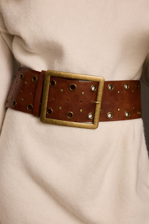 Faux leather belt in cognac with brass square buckle and grommet stud detail, on cream knit dress