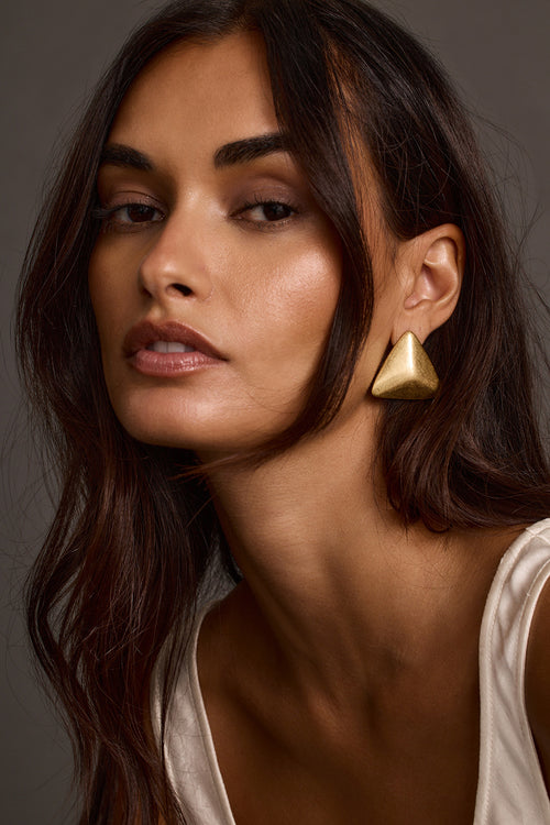 Close-up portrait of woman wearing gold statement earrings and beige top