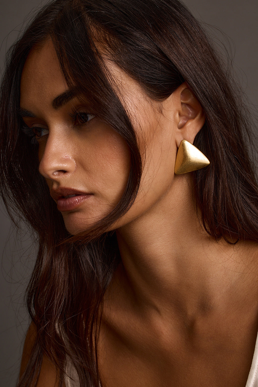 Woman wearing gold statement earrings, close-up portrait side view