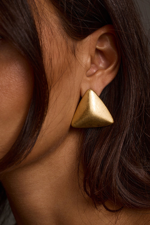 Close-up of gold statement earrings with triangular stud design, worn on ear