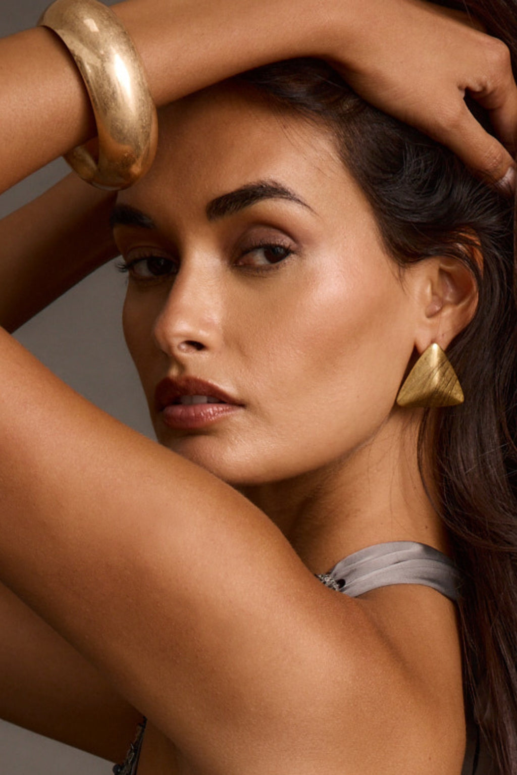 Close-up of a woman wearing a triangular gold statement earring and a chunky gold bangle