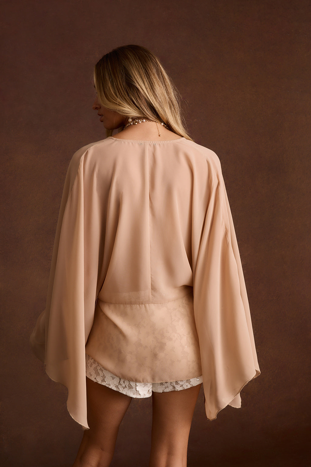 Back view of a sheer nude cape-sleeve top over lace shorts.