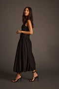 Woman walking in a sleeveless black midi dress with strappy high-heeled sandals